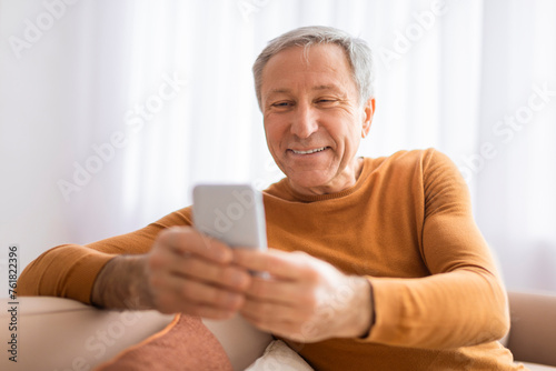 Older man viewing smartphone with pleasant smile