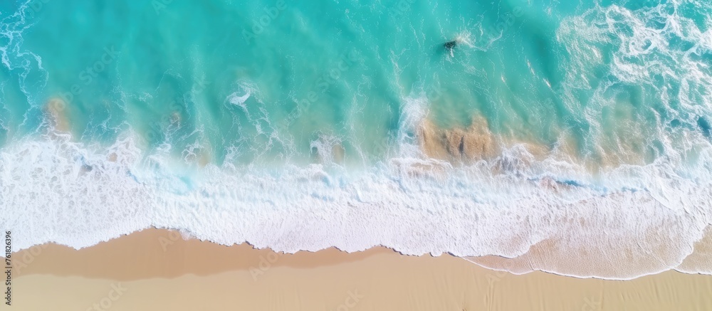 An aerial view of a sandy beach with azure waves crashing on the shore, creating a beautiful fluid pattern in the landscape - obrazy, fototapety, plakaty 