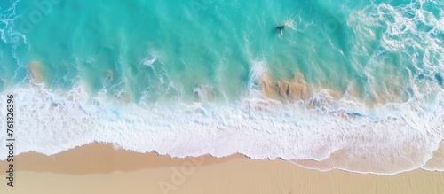 An aerial view of a sandy beach with azure waves crashing on the shore, creating a beautiful fluid pattern in the landscape