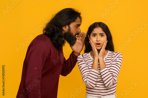 Man whispers secret to surprised woman on yellow