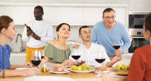 Ethnically diverse group of cheerful adult women and men engaging in casual banter and enjoying friendly company over wine 