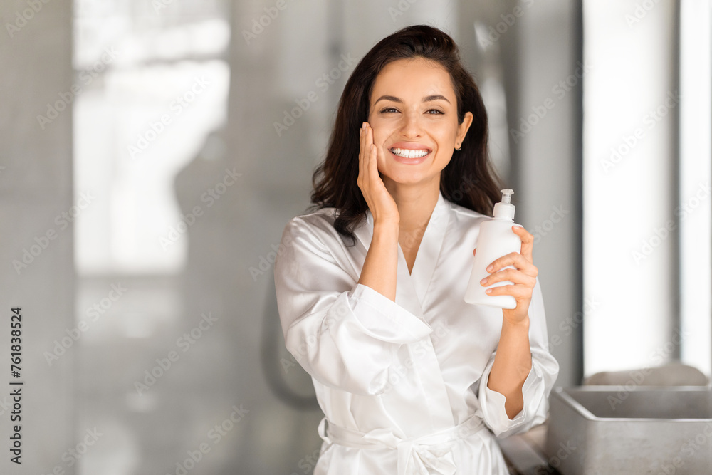 Cheerful young brunette woman holding bottle with face cream Cheerful young brunette woman holding bottle with face cream
