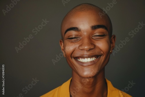 Non-binary person with a shaved head and a yellow shirt is smiling © top images