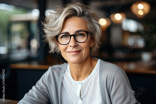 Elegant older woman in glasses smiling warmly at her office desk.