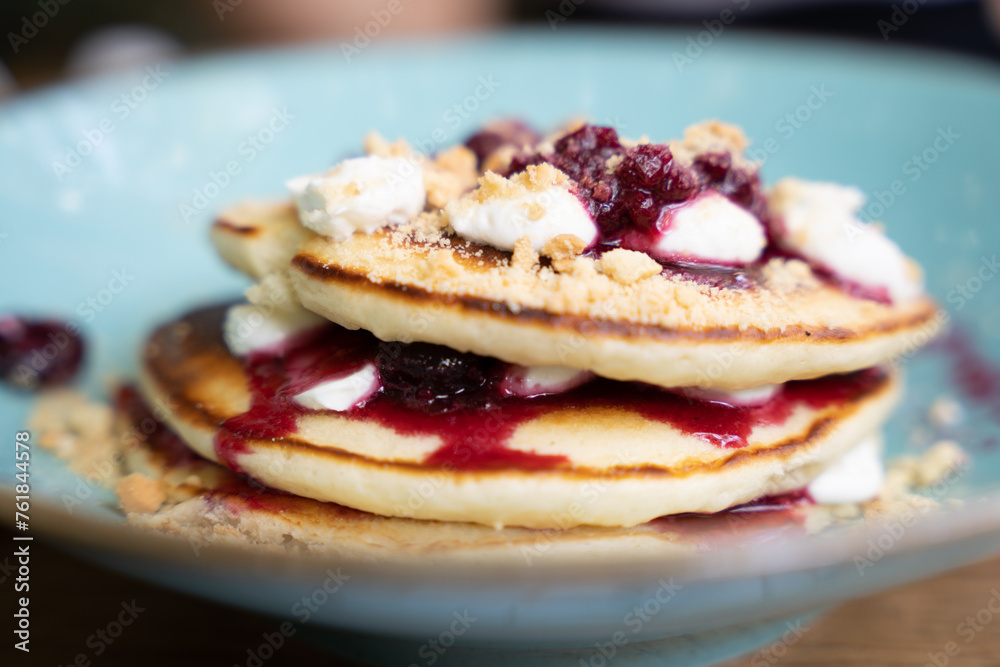 Close-up of pancakes with berry compote and cream on a blue plate Close-up of pancakes with berry compote and cream on a blue plate