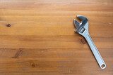 A wrench lays flat on top of a simple wooden table, casting a shadow in the light.