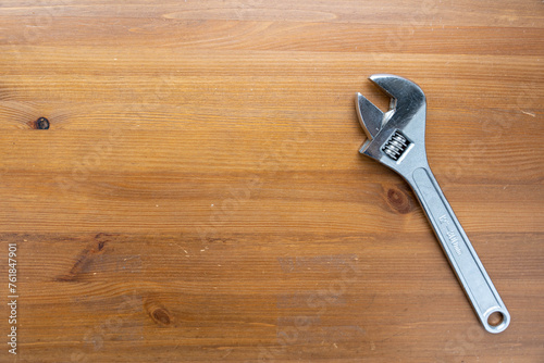 A wrench lays flat on top of a simple wooden table, casting a shadow in the light.