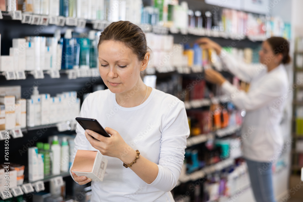 In pharmacy female visitor scan QR Code and reads composition of cream for problematic teenage skin. Mom picks up cream for adolescent daughter in cosmetics department