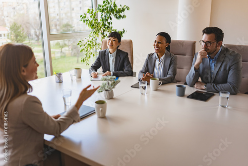 A diverse group of multi-ethnic businesswomen sit in a corporate office and have a meeting with a business associate photo
