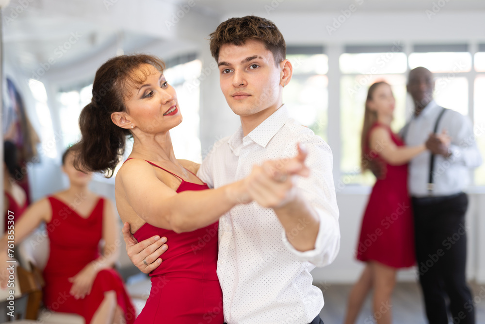 Fototapeta premium Pretty young woman dancing waltz with partner at group of multinational people in modern ballroom dancing class
