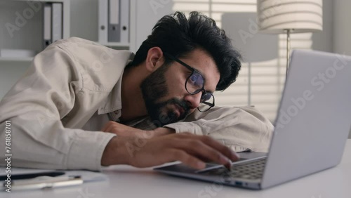Tired sleepy exhausted Arabian Indian business man drowsy frustrated businessman worker employee sad fatigued lazy male guy sleep sleeping at office desk with laptop boring computer work overwork nap