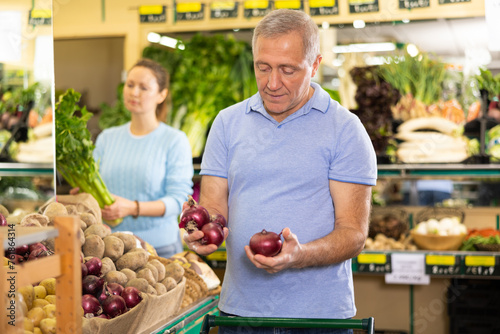 Busy focused casual elderly man buying local red onions for salad during shopping in grocery store