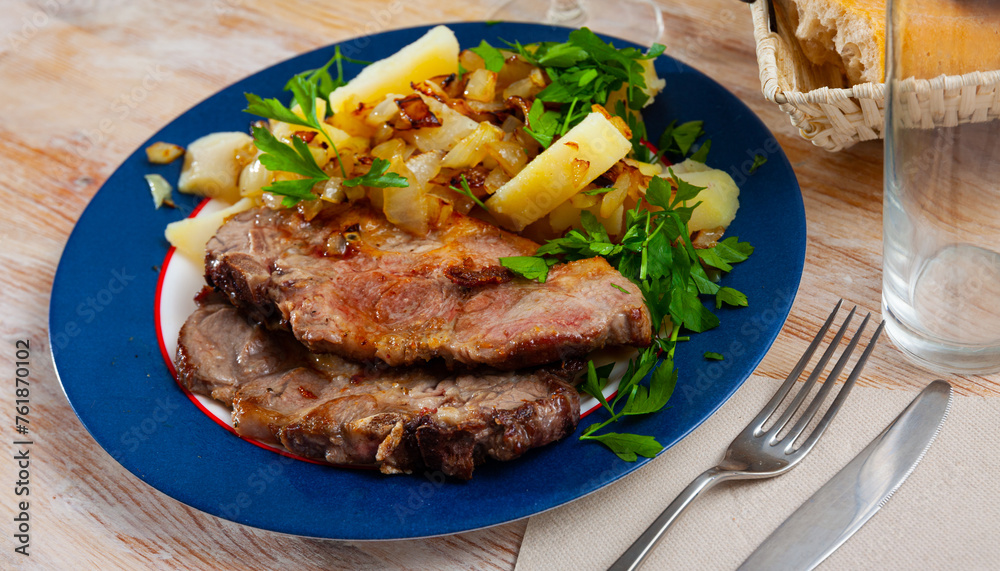Appetizing fried pork with potatoes and herbs closeup