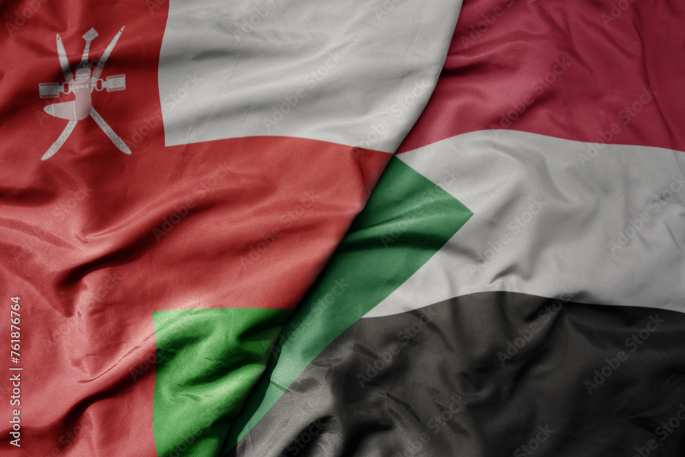 big waving national colorful flag of sudan and national flag of oman.