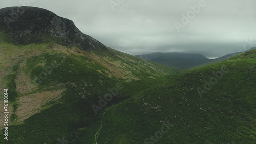 Scottish mountain ranges aerial view: path between green hills. Grey clouds wrapped top of mounts in summer day. Wild untouched nature scenery of island Arran. Footage Shot in 4K (UHD)
