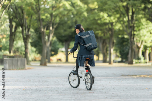 公園の中を自転車通学する制服姿の中学生・高校生の女の子
