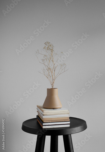 Still life of vintage books and ceramic vase with small yellow dried flowers on a small black table