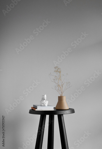 Still life of vintage books, white sculpture bust, and ceramic vase with small yellow dried flowers on a small black table