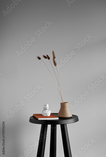Still life of vintage book, white sculpture bust, and ceramic vase with brown Foxtail stems on a small black table