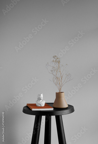 Still life of vintage book, white sculpture bust, and ceramic vase with small yellow dried flowers on a small black table