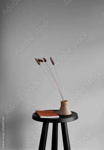 Still life of vintage book and ceramic vase with brown Foxtail grass stems on a small black table