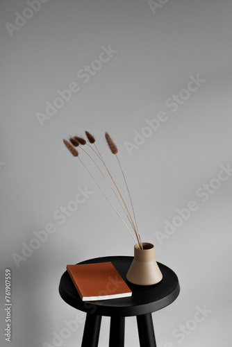Still life of vintage book and ceramic vase with brown Foxtail grass stems on a small black table