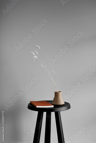 Still life of vintage book and ceramic vase with white Foxtail grass stems on a small black table