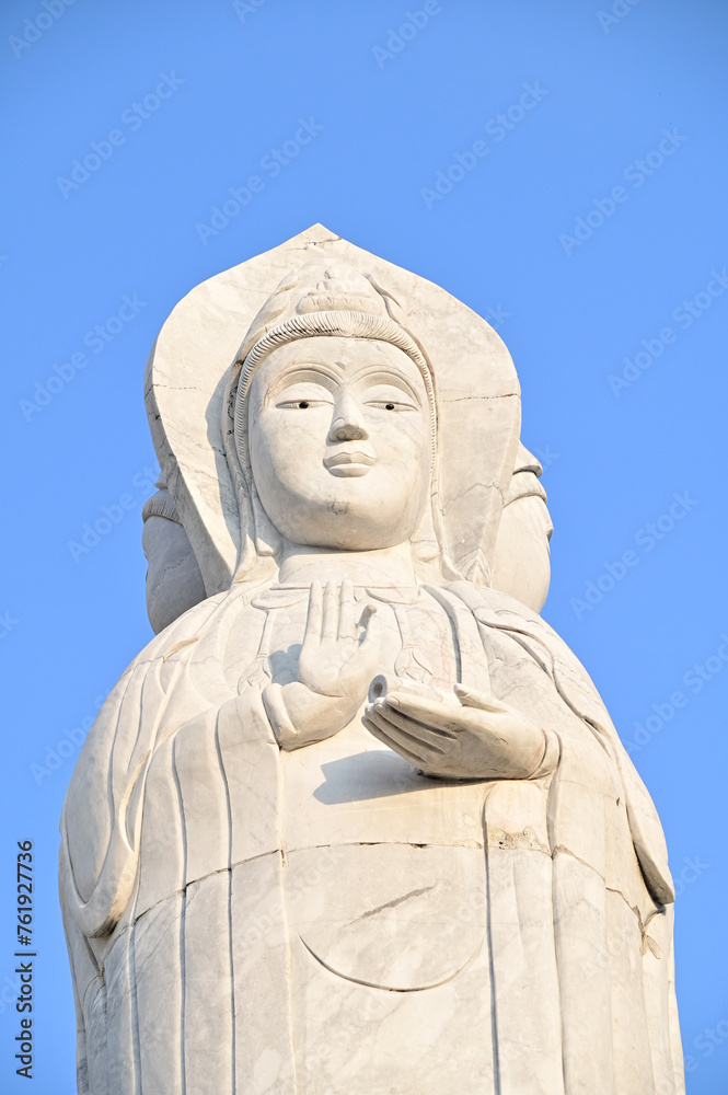 Closeup of The White Guan Yin Statue is the Bodhisattva of Mahayana Buddhism standing in a beautiful Thai Buddhist temple at Thailand with blue sky background.