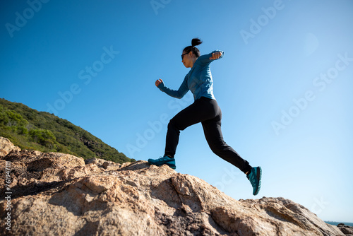 Woman runner running on sunrise seaside rocky mountains