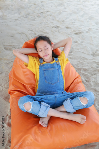 Portrait of Asian young girl in dungarees jean relax and sleeping on orange sofa bed beach on sand at summer holiday.