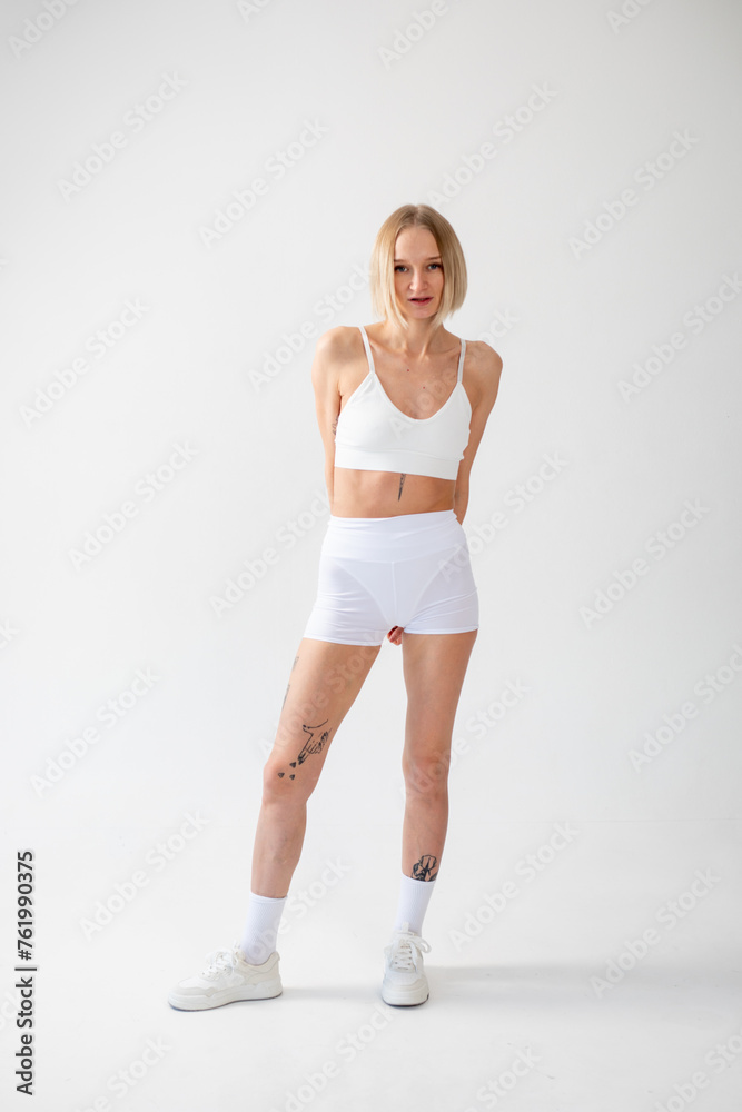 Blonde girl posing on a white background in a top and leggings