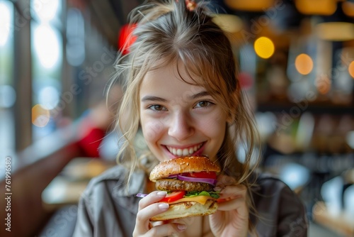 Young Woman Enjoying Delicious Cheeseburger with a Smile in a Trendy Restaurant with Warm Ambiance