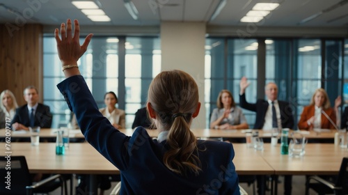 Rear view photo of a businesswoman raising one arm in a conference meeting asking question in casual attire in front of a business professional crowd