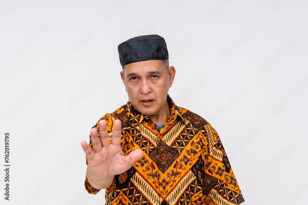 A composed middle-aged Indonesian man wearing a batik shirt and kopiah hat tells someone to calm down. Isolated on white. A composed middle-aged Indonesian man wearing a batik shirt and kopiah hat tells someone to calm down. Isolated on white.
