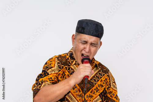 An Indonesian man in traditional batik shirt and kopiah hat passionately singing during a karaoke session. Isolated on a white background. photo