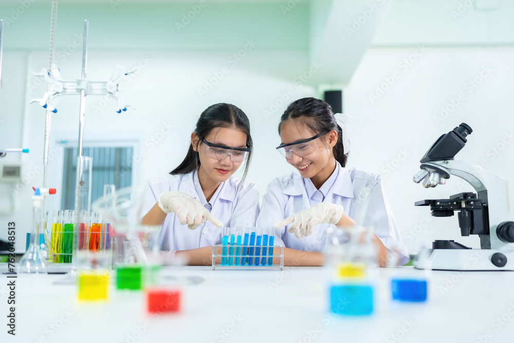 Two Asian female scientists from the World Pharmacy Organization Test tubes are being used to make drugs and vaccines. There is a microscope. Blue melted lines from cells in a research lab Two Asian female scientists from the World Pharmacy Organization Test tubes are being used to make drugs and vaccines. There is a microscope. Blue melted lines from cells in a research lab