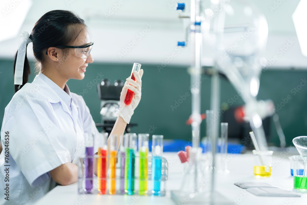 Side view of Asian female doctor researching a vaccine in a biolab holding a red test tube as medicine. Do scientific work in medical and pharmaceutical industry companies and use microscopes. Side view of Asian female doctor researching a vaccine in a biolab holding a red test tube as medicine. Do scientific work in medical and pharmaceutical industry companies and use microscopes.