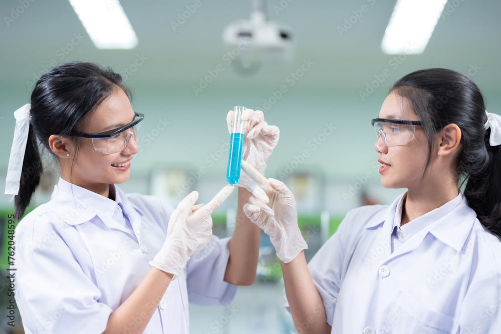 Closeup of two Asian female chemists holding chemical test tubes inside with blue solution. To conduct research in the science lab of the Faculty of Pharmacy at the university to produce medicines. Closeup of two Asian female chemists holding chemical test tubes inside with blue solution. To conduct research in the science lab of the Faculty of Pharmacy at the university to produce medicines.