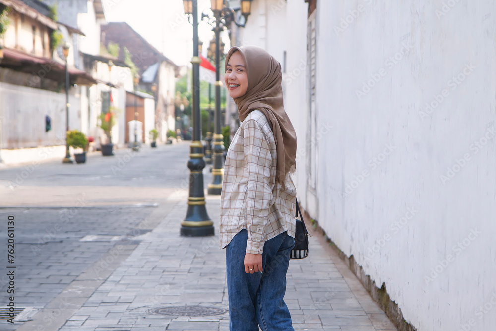 back view of smiling happy asian muslim woman roaming around kota lama or old city area, Semarang, Central Java , Indonesia. Traveling concept