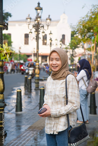happy asian muslim woman standing beside the street and smiling. roaming around kota lama or old city area, Semarang, Central Java , Indonesia. Traveling concept
