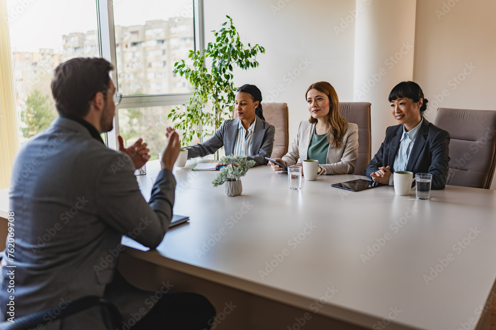 A diverse group of multi-ethnic businesswomen sit in a corporate office and have a meeting with a business associate A diverse group of multi-ethnic businesswomen sit in a corporate office and have a meeting with a business associate