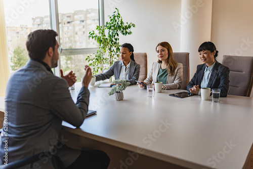 A diverse group of multi-ethnic businesswomen sit in a corporate office and have a meeting with a business associate