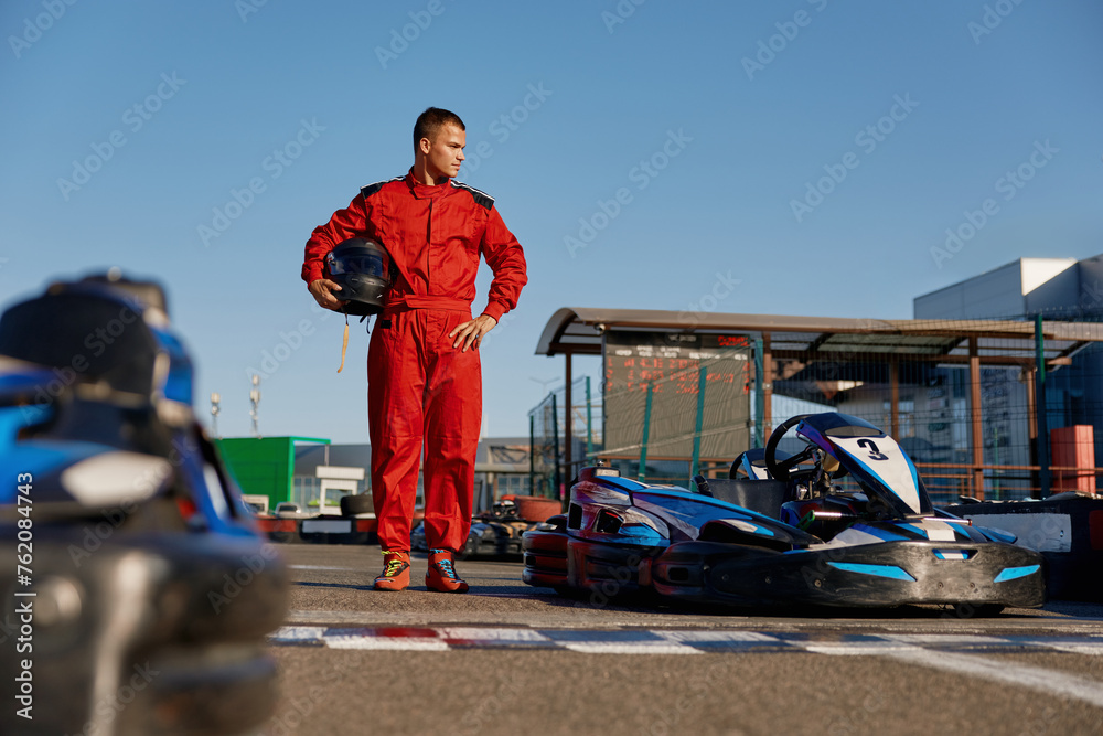Go-kart driver walking to car before race at starting line on motor racing track - obrazy, fototapety, plakaty 