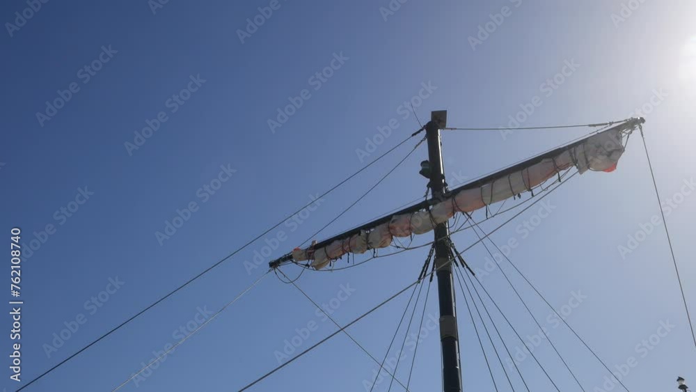 Pirate ship mast and furled sails stand against a clear sky, sunbeams casting a glow, perfect for themes of sailing adventure and discovery