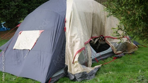 A man pitching a tent and dropping a tent pole. The bald male is wearing shorts in a field whilst camping