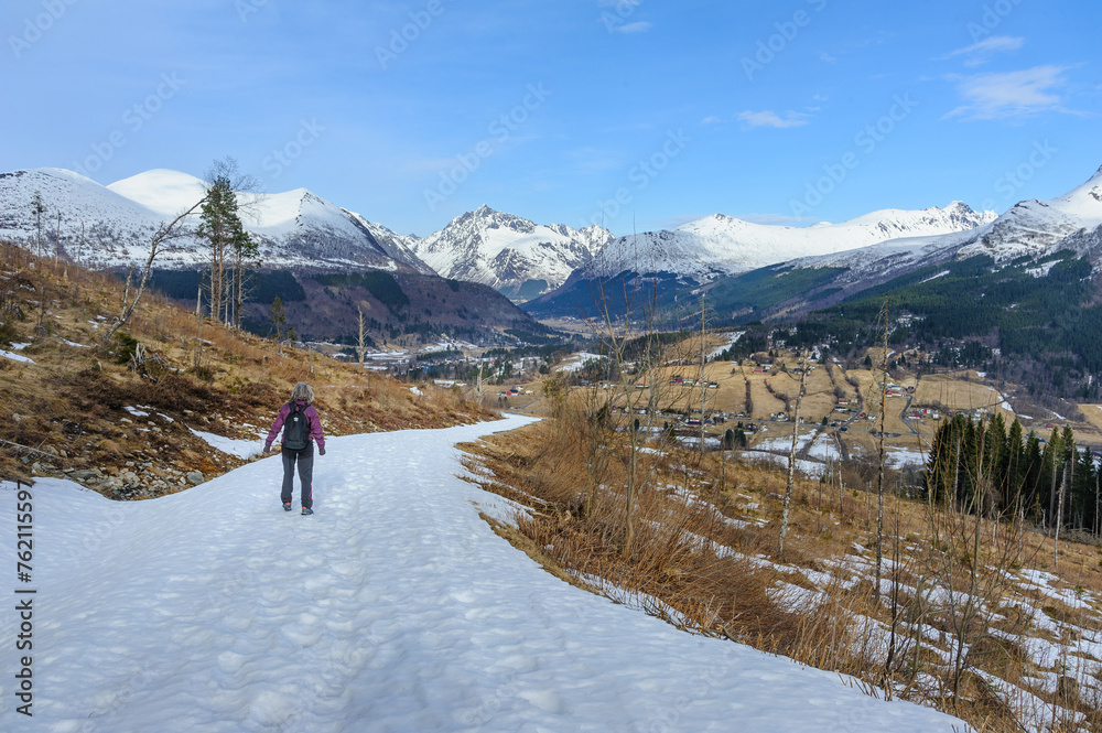 A solitary hiker makes their way along a snowy trail with mountain scenery in the background.