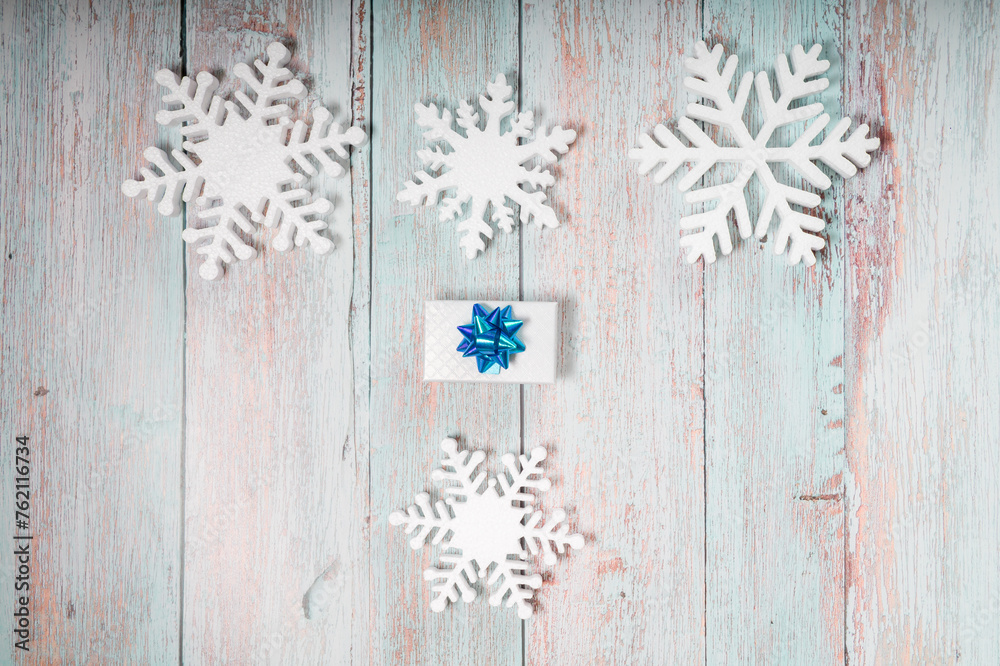 Snowflakes and a present with blue ribbon on a light blue wooden background. Christmas winter flatlay with copyspace	