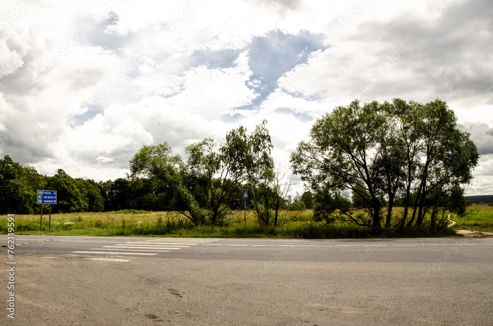 Asphalt road in the countryside with trees and clouds in the sky
