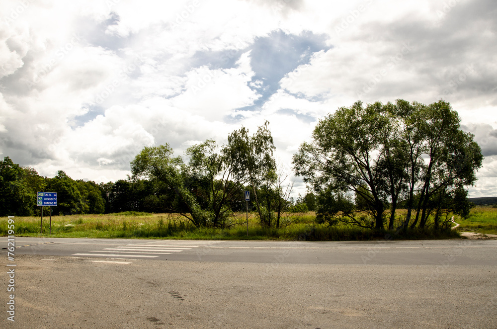 Asphalt road in the countryside with trees and clouds in the sky Asphalt road in the countryside with trees and clouds in the sky