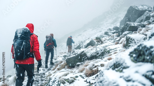 Group of hikers climbing rocky mountain in high altitude in freezing foggy and snowy weather. Physical challenge, endurance and perseverance.
